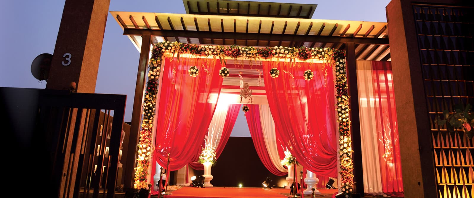 Decorated red-and-gold open-air wedding mandap entrance lit up at night at Montecristo Banquet, Ahmedabad
