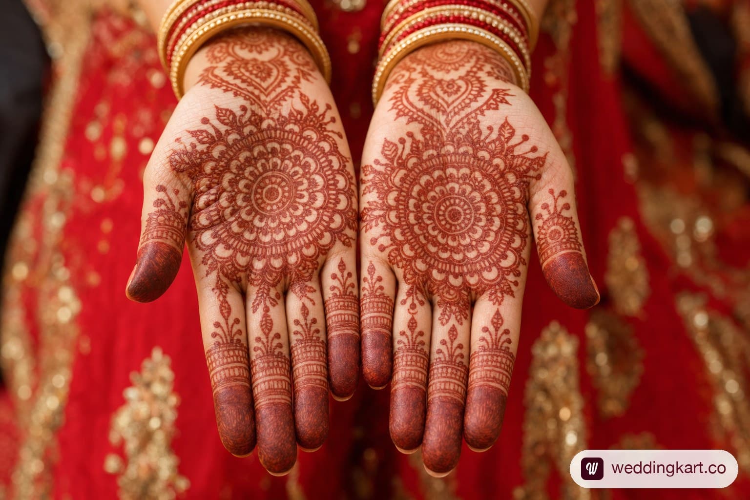Front hand mehndi design on bridal palms: grand circular mandala at each palm centre with striped fingertip caps, deep reddish-brown stain