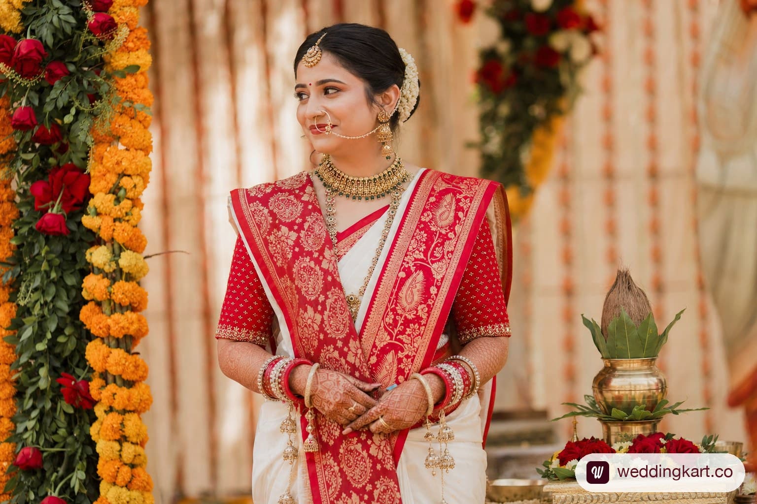 Gujarati bride in traditional white and red Panetar silk saree with seedha pallu drape at a decorated wedding mandap with marigold and rose decor